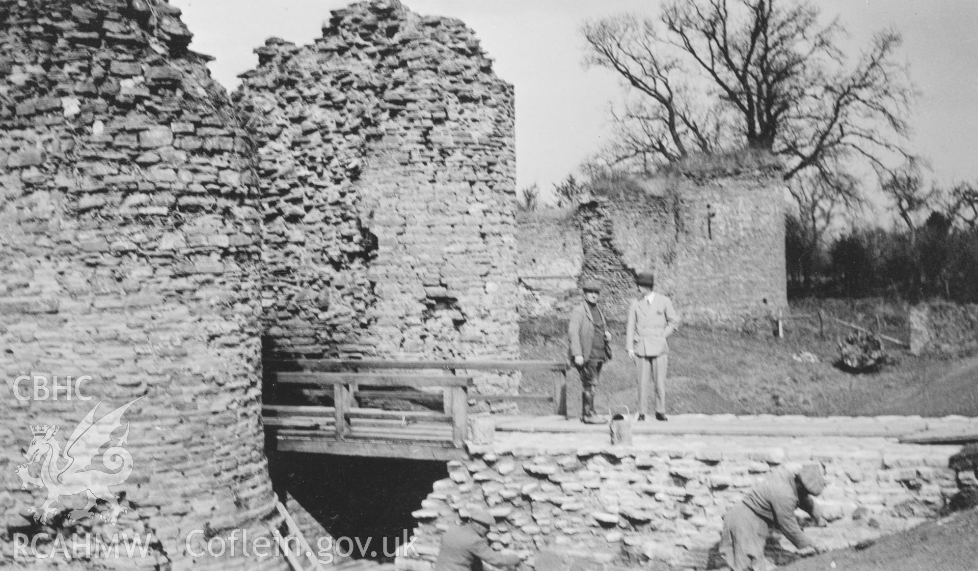View of access bridge and towers during restoration, White Castle, Llantilio.  Three workmen and one other figure captured on the image.  Dated March 1934.