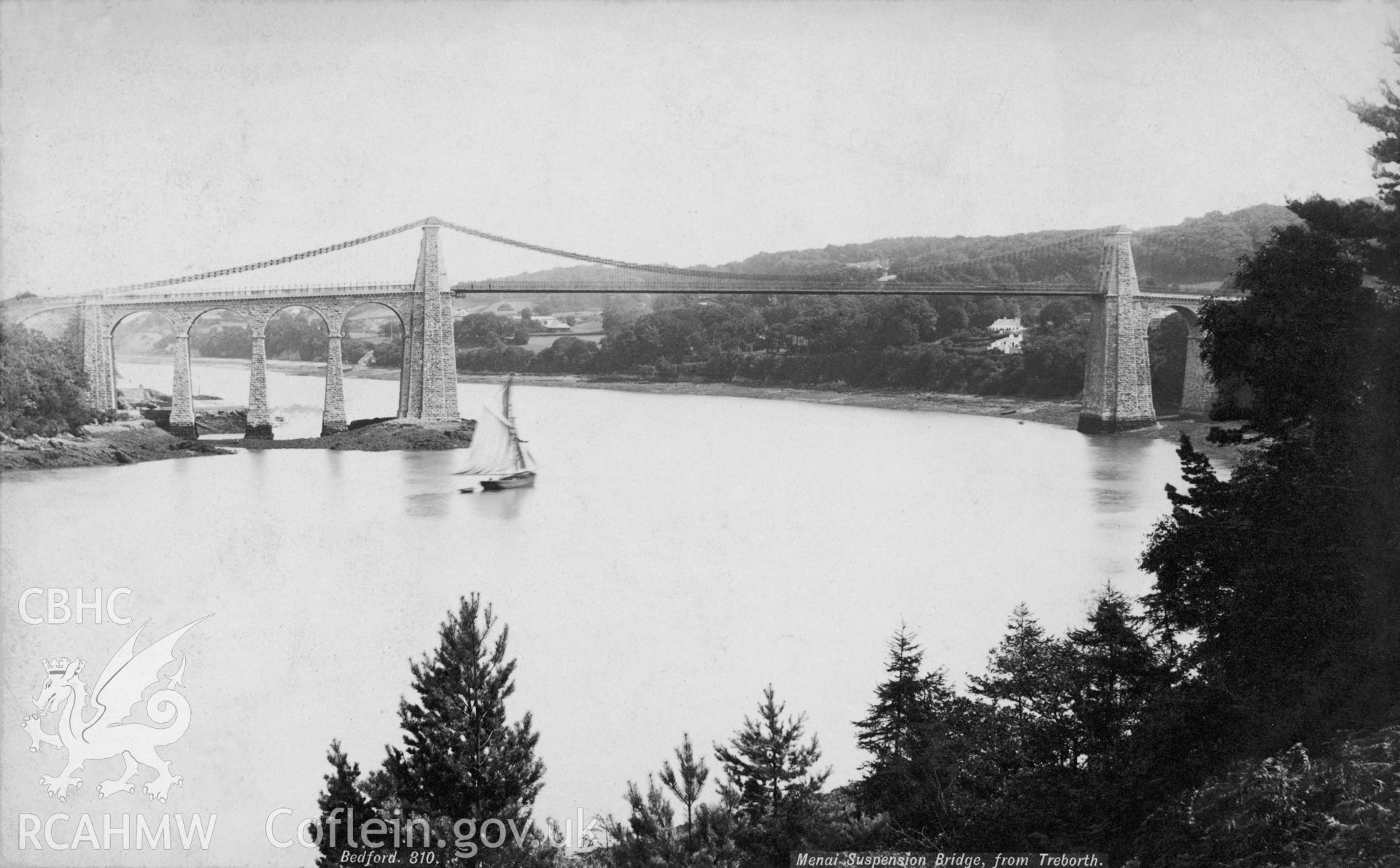 Black and white print of Menai Suspension Bridge, Menai Bridge, showing the bridge from the Treborth side with a gaff rigged sloop sailing underneath.