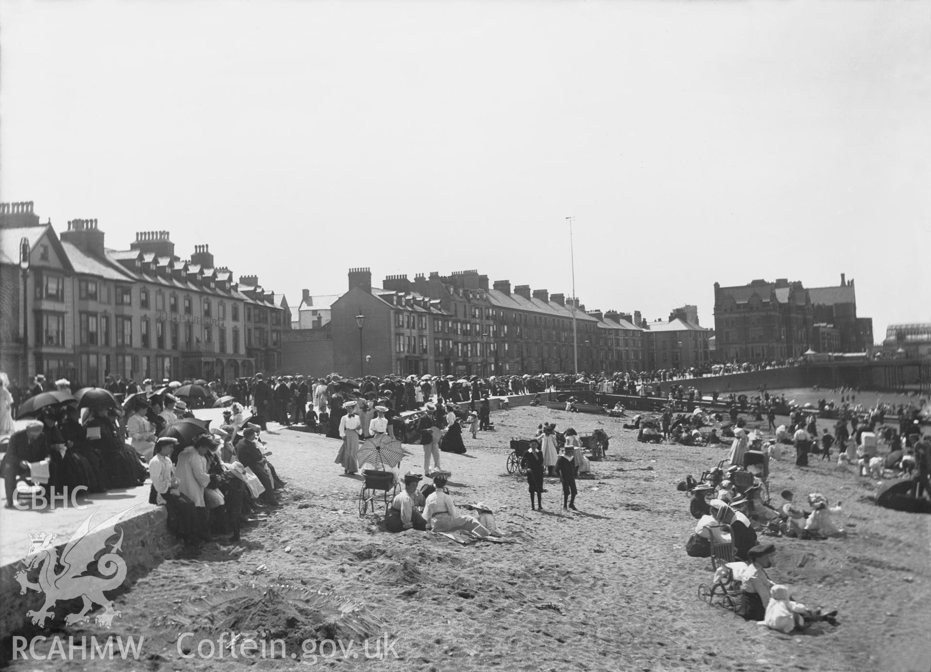 Black and white image dating from c.1910 showing a busy beach scene at Aberystwyth with Marine Terrace in the background.