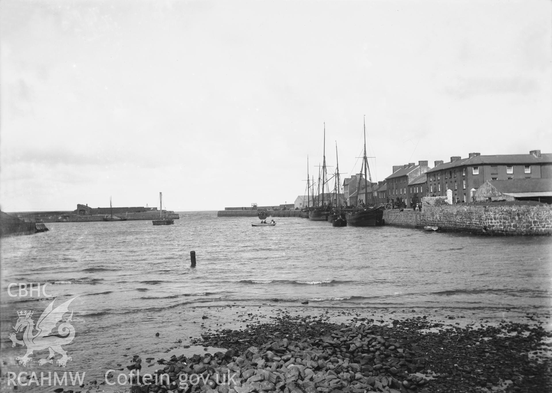 Black and white image dating from c.1910 showing the harbour in Aberaeron taken from inland, buildings in Cadwgan Place and Pen Cei are visible on the right and a number of sailing vessels are moored on the quay.