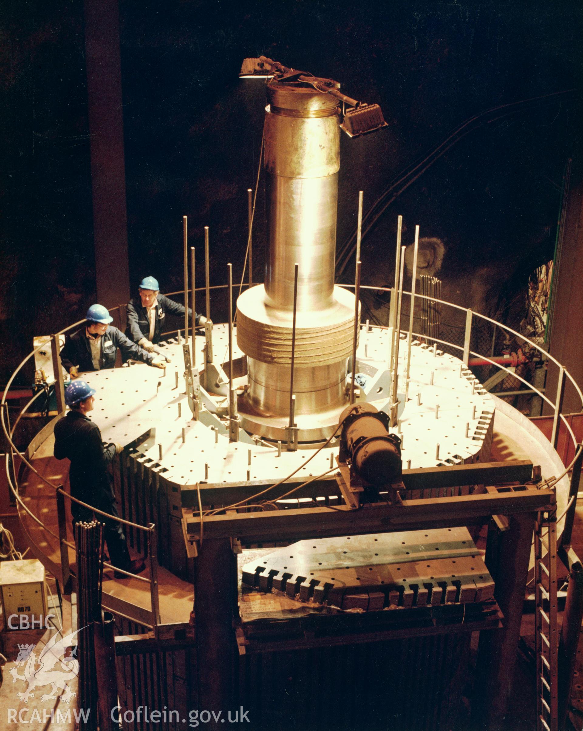 1 colour print showing assembly work on one of the reversible generator motors on top of the main shaft at Dinorwig Power Station; collated by the former Central Office of Information.