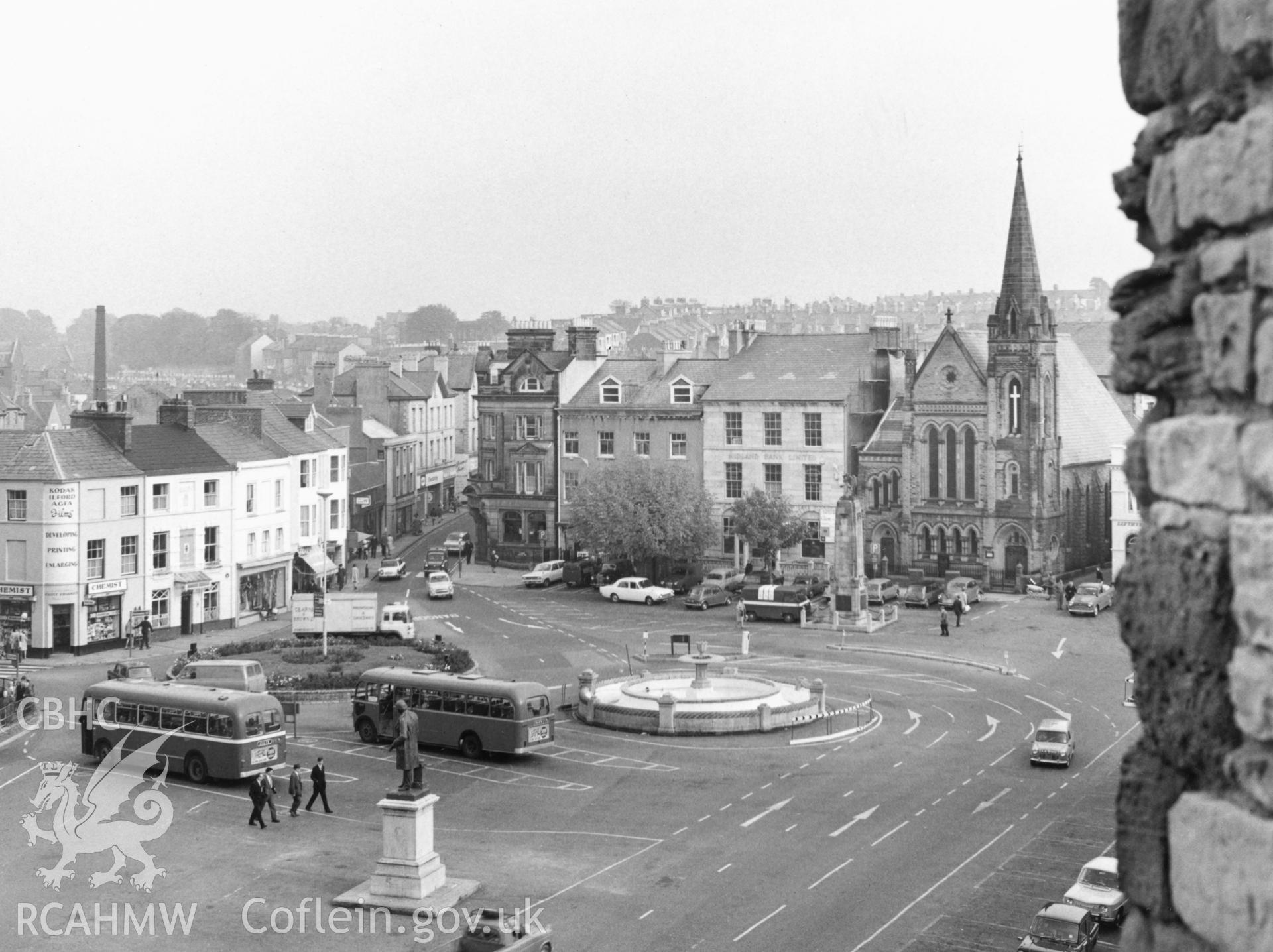 1 b/w print showing view of Y Maes, Caernarfon from the castle walls with cars and buses; collated by the former Central Office of Information.