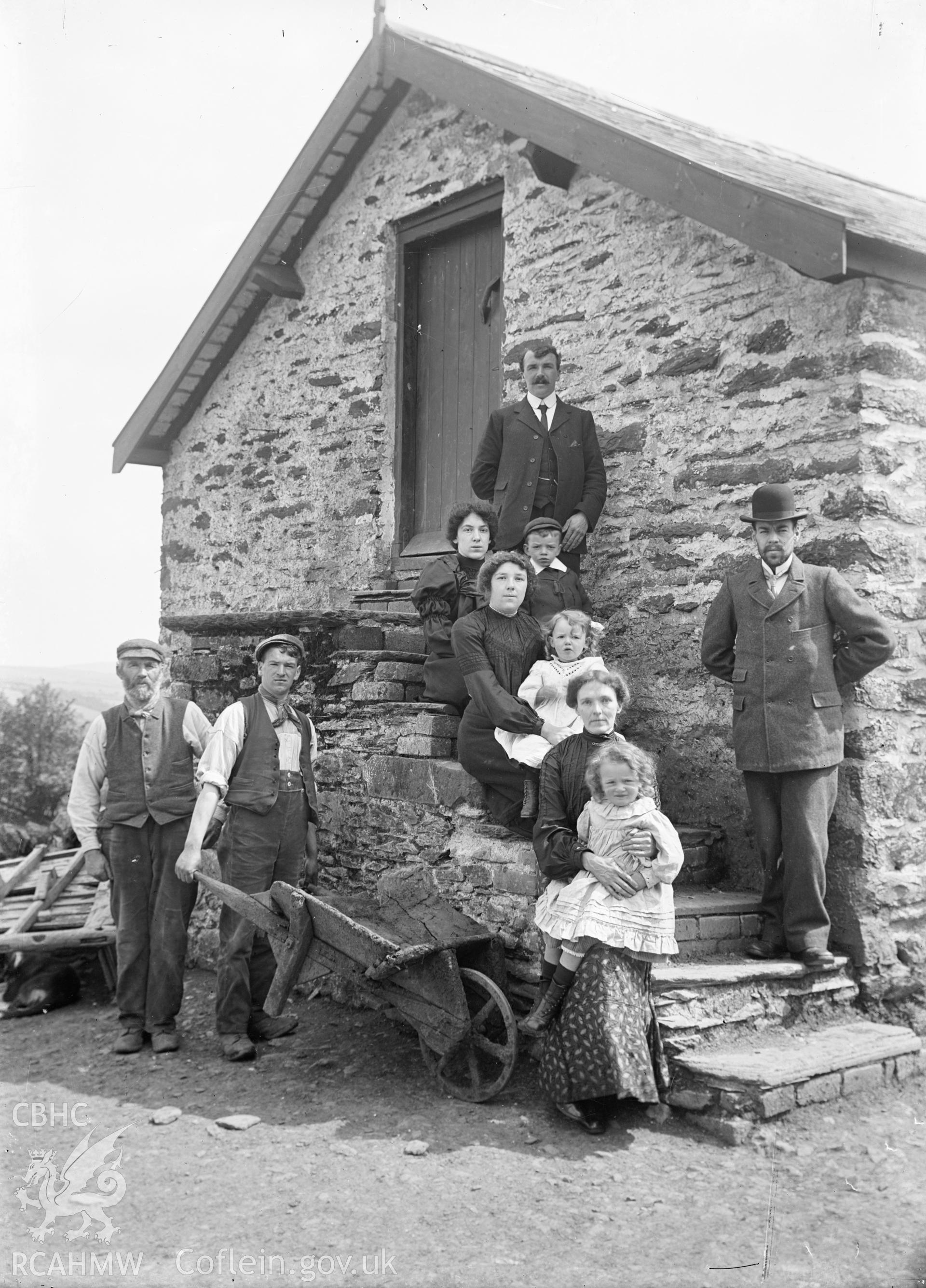 Black and white glass negative showing family group on the steps of a farm outbuilding.