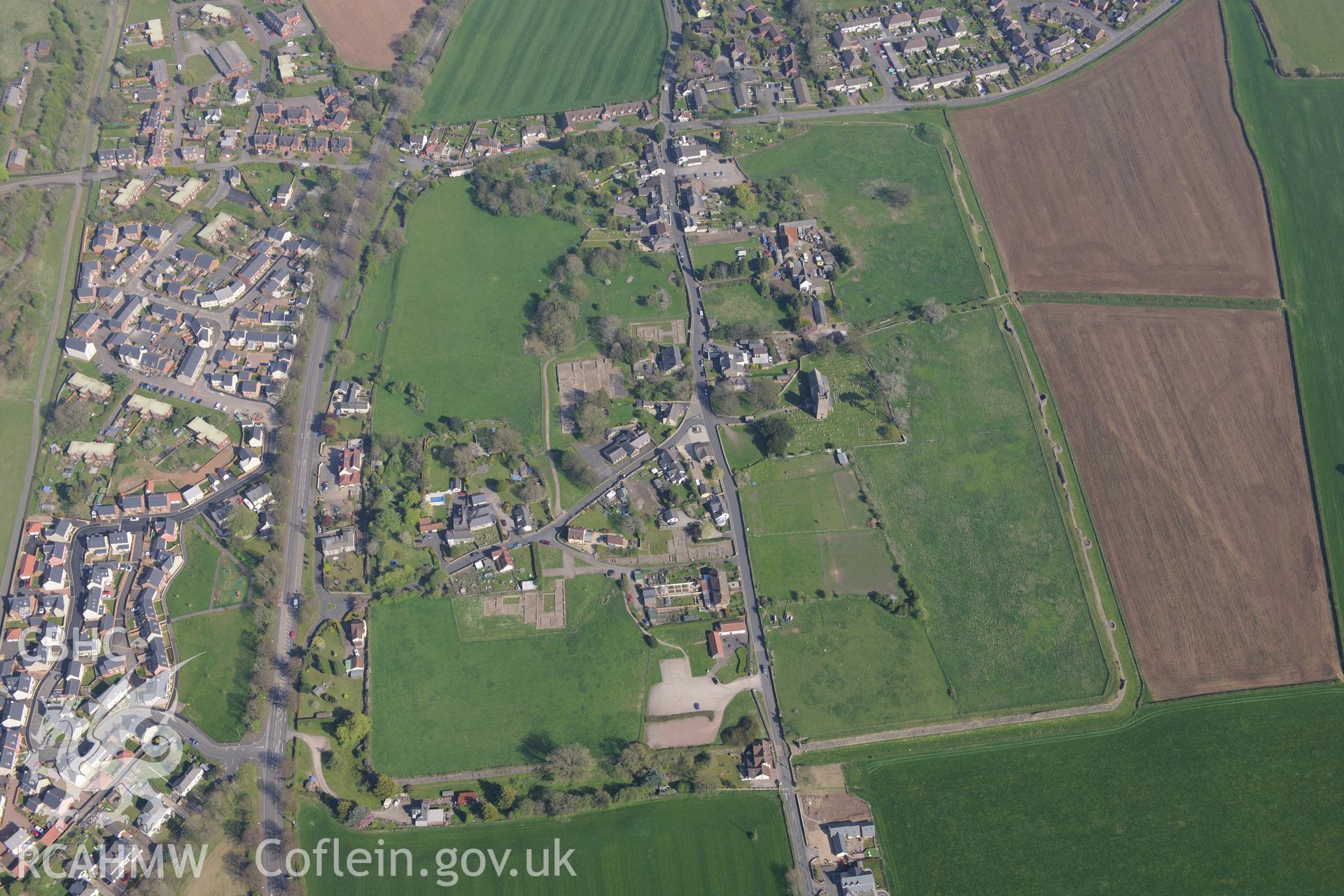 Caerwent village and Roman city including views of the Roman Amphitheatre and Basilica and Forum; St. Stephen's Church; Caerwent Baptist Chapel; Caerwent House; Great House; Caerwent Institute and West Gate Farm. Oblique aerial photograph taken during the Royal Commission's programme of archaeological aerial reconnaissance by Toby Driver on 21st April 2015.