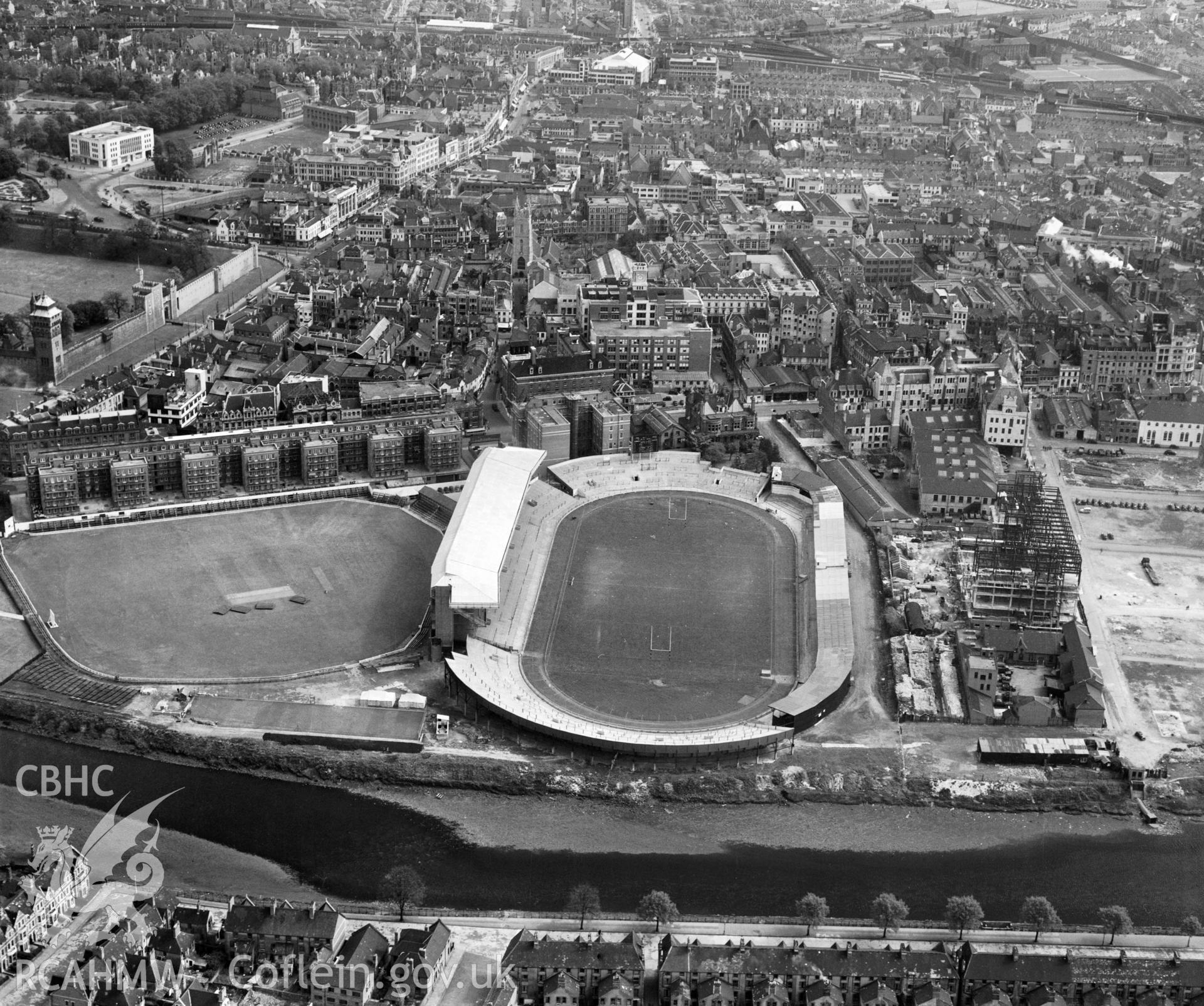 Digital copy of a black and white, oblique aerial photograph of Cardiff Arms Park, Cardiff. The photograph shows a view from the West following the completion of the North Stand. On the right hand side of the photograph it iss possible to see Empire House, a telephone exchange, under construction on the site of the Temperance Town which was demolished by the Cardiff Corporation in 1937.