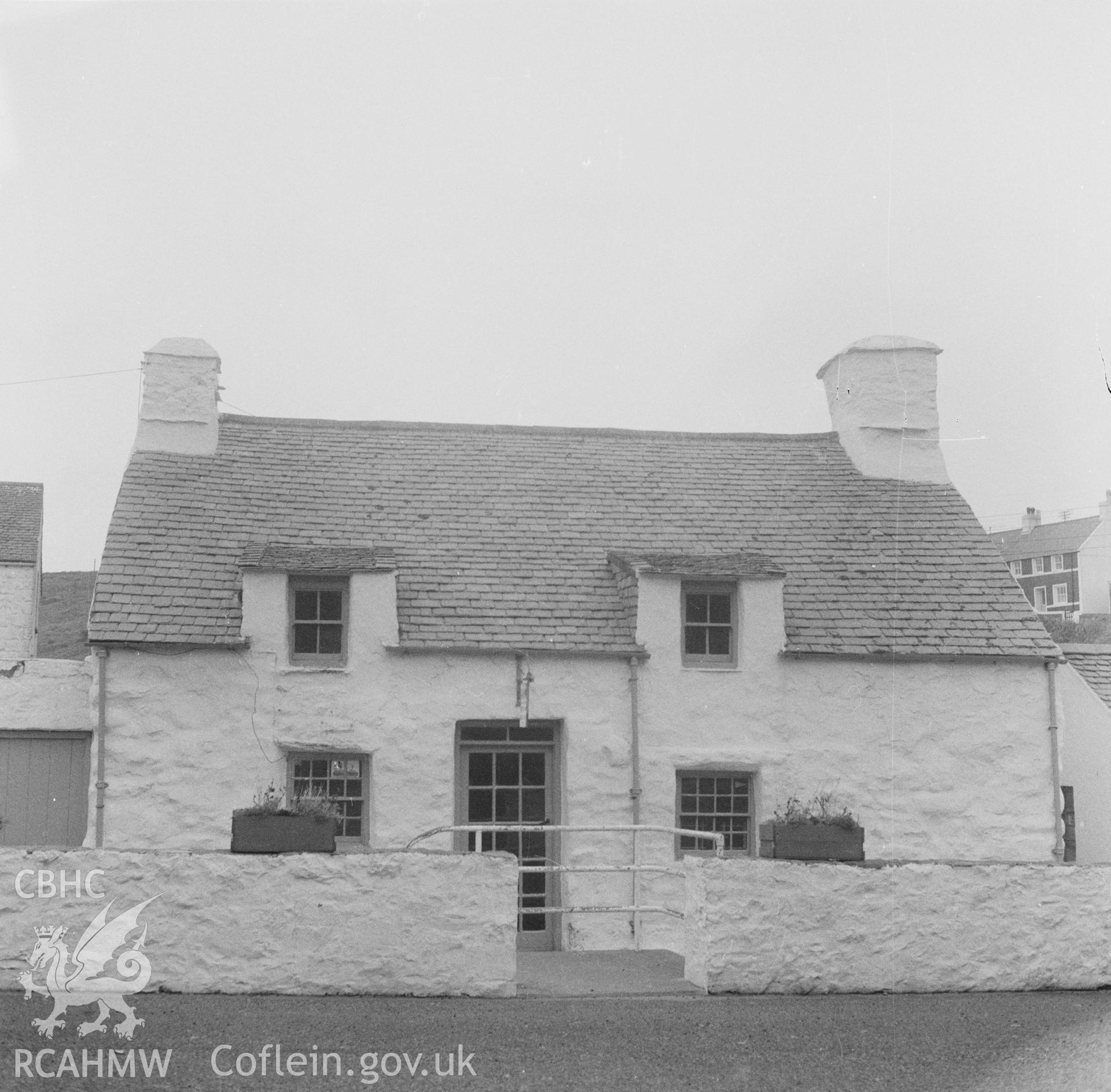 Digital copy of a black and white nitrate negative showing an exterior view of unidentified cottages, captioned 'Caernarfon Cottages'.