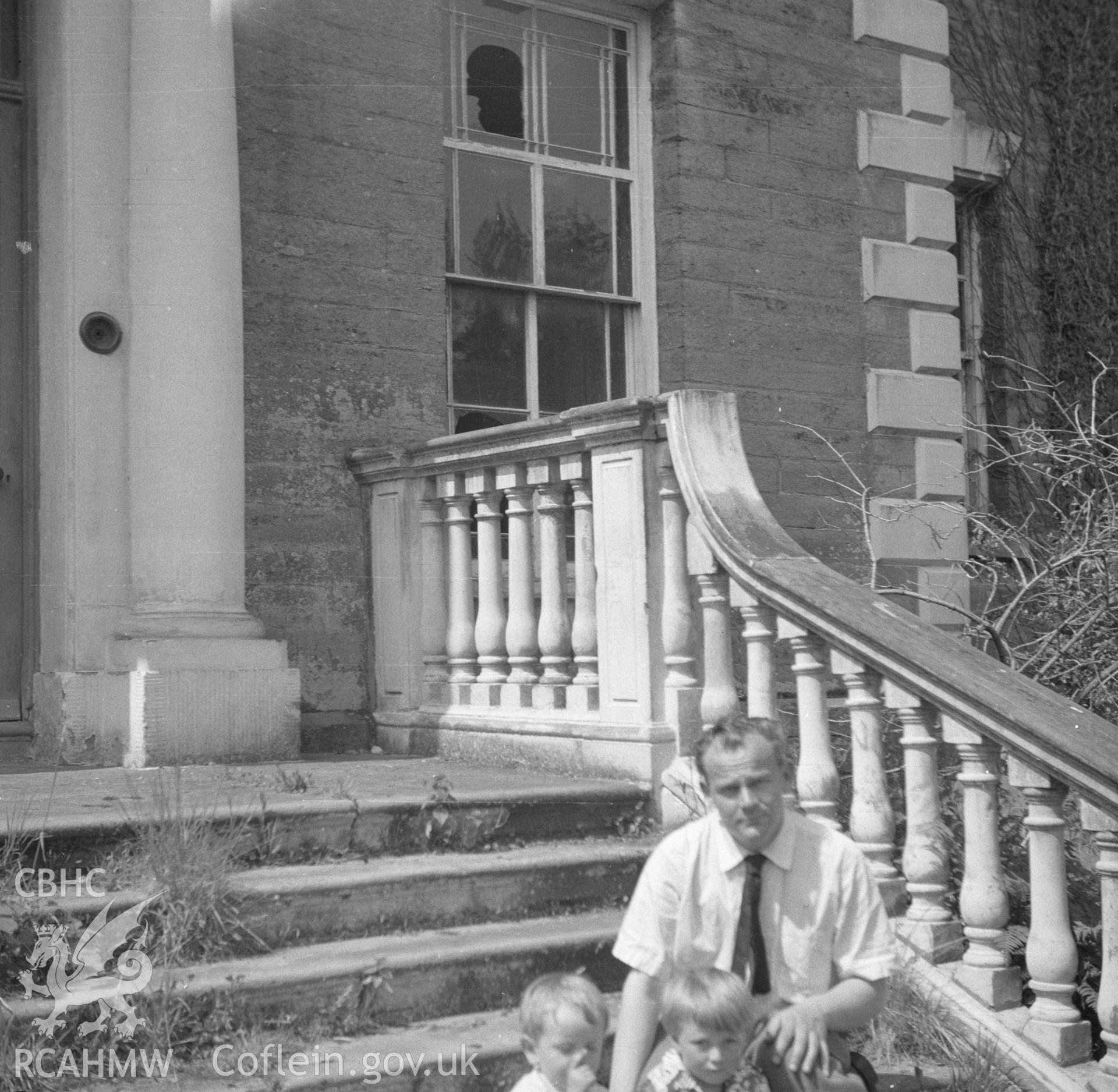 Digital copy of a black and white nitrate negative, exterior elevation of Ynysmaengwyn, with three figures sitting on the front steps.