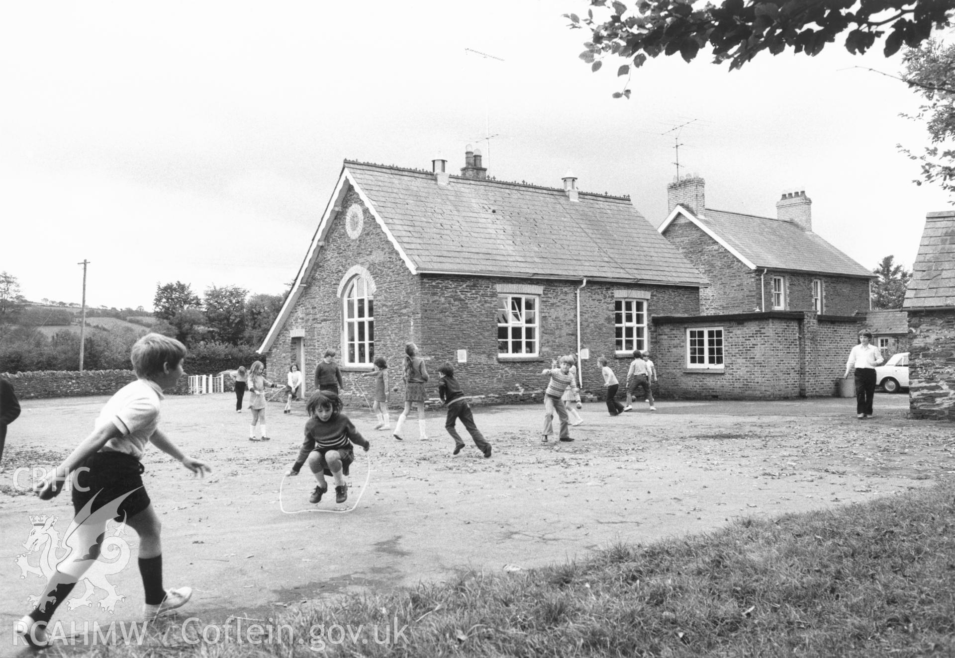 1 b/w print showing exterior view of the primary school, Llangybi (Monmouthshire) with children playing; collated by the former Central Office of Information.
