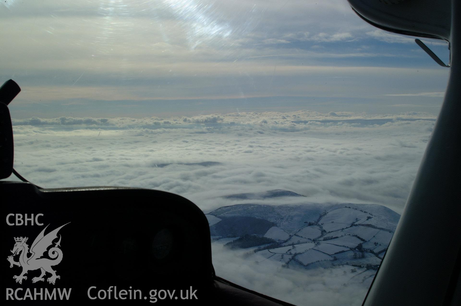 RCAHMW colour oblique aerial photograph of hills and commons south of Llananno, viewed from the north under snow and freezing fog, through the aircraft windscreen. Taken on 19 November 2004 by Toby Driver